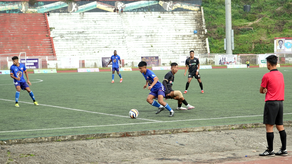Players of Sechü Zubza FC (in blue) and Ward-19 (in black) battle for possession during their hard-fought encounter at IG Stadium, Kohima, in the 25th NSF Martyrs’ Memorial Trophy 2025. SZFC advanced to the quarterfinals after a tense penalty shootout, thanks to captain Neithovilie Chalieu’s heroic saves.